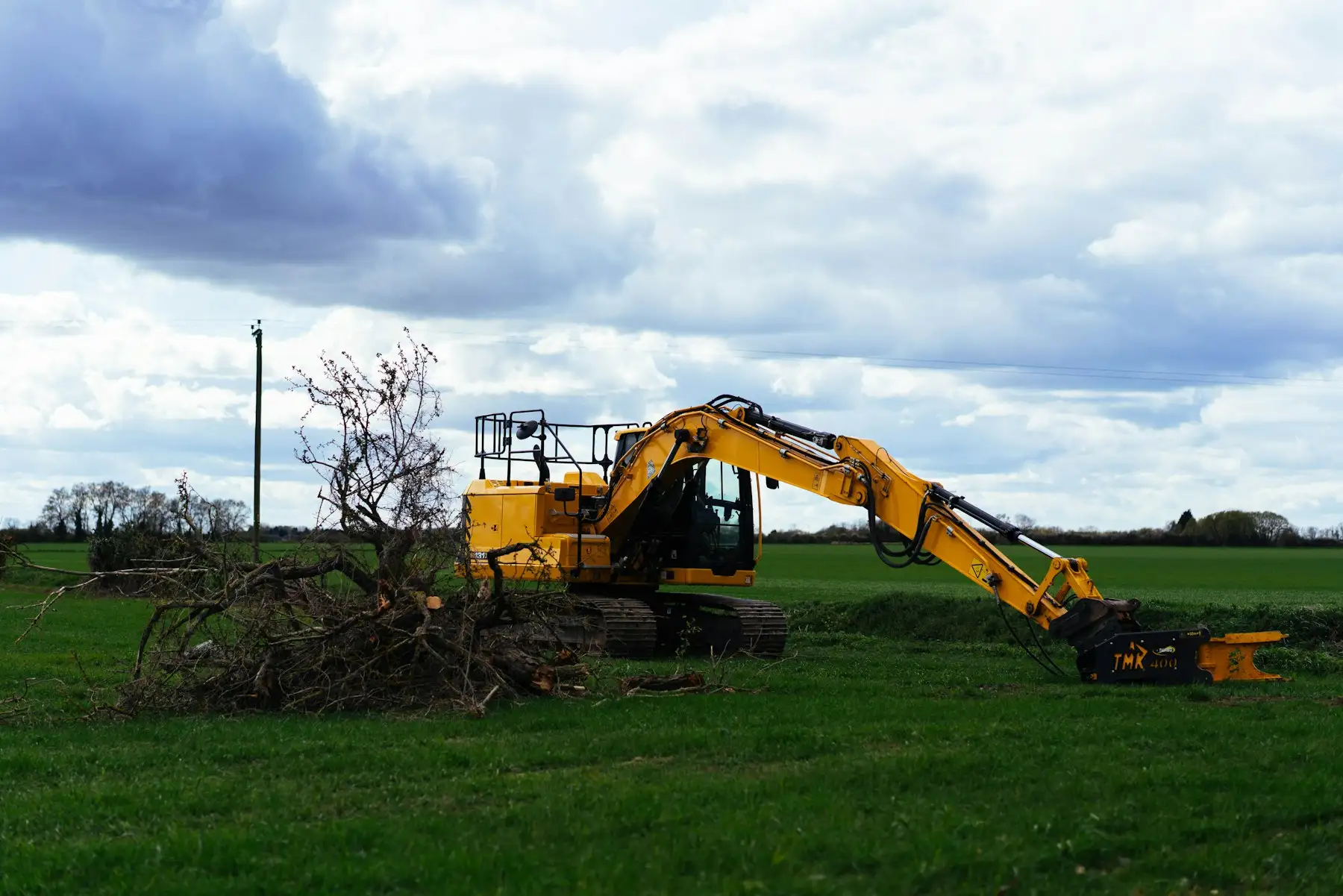 Excavator clearing cut brush and branches out of an overgrown field