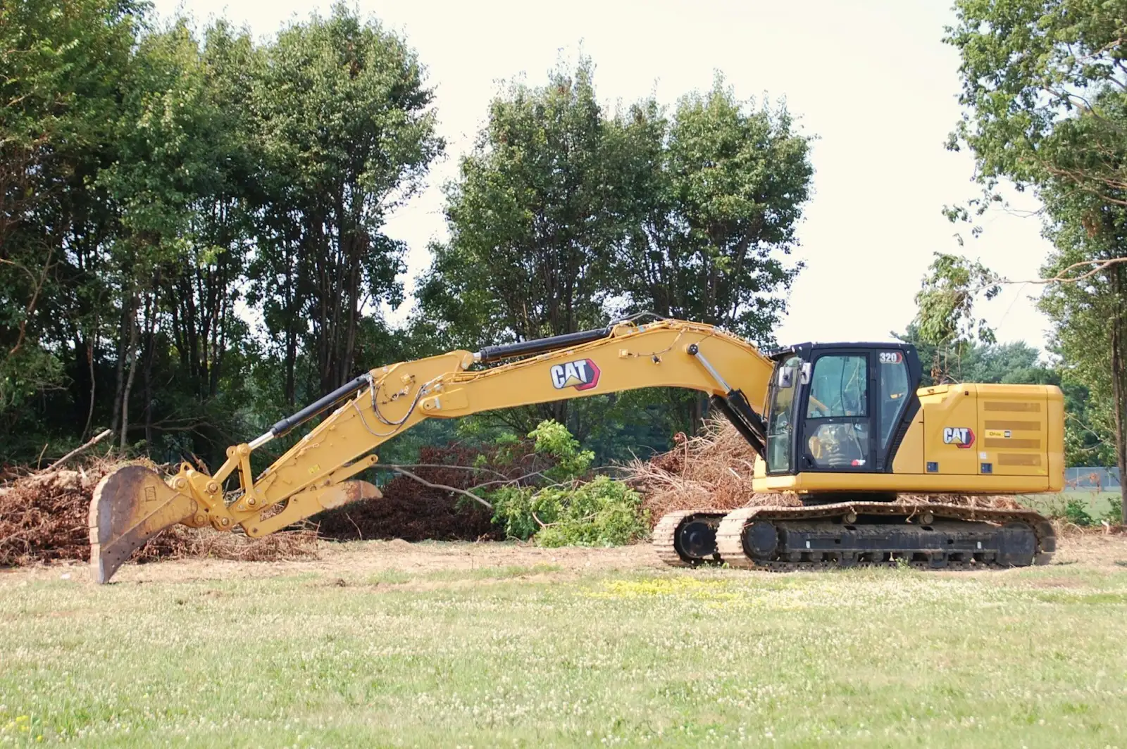 Excavator parked on grass at the edge of trees and heavy brush
