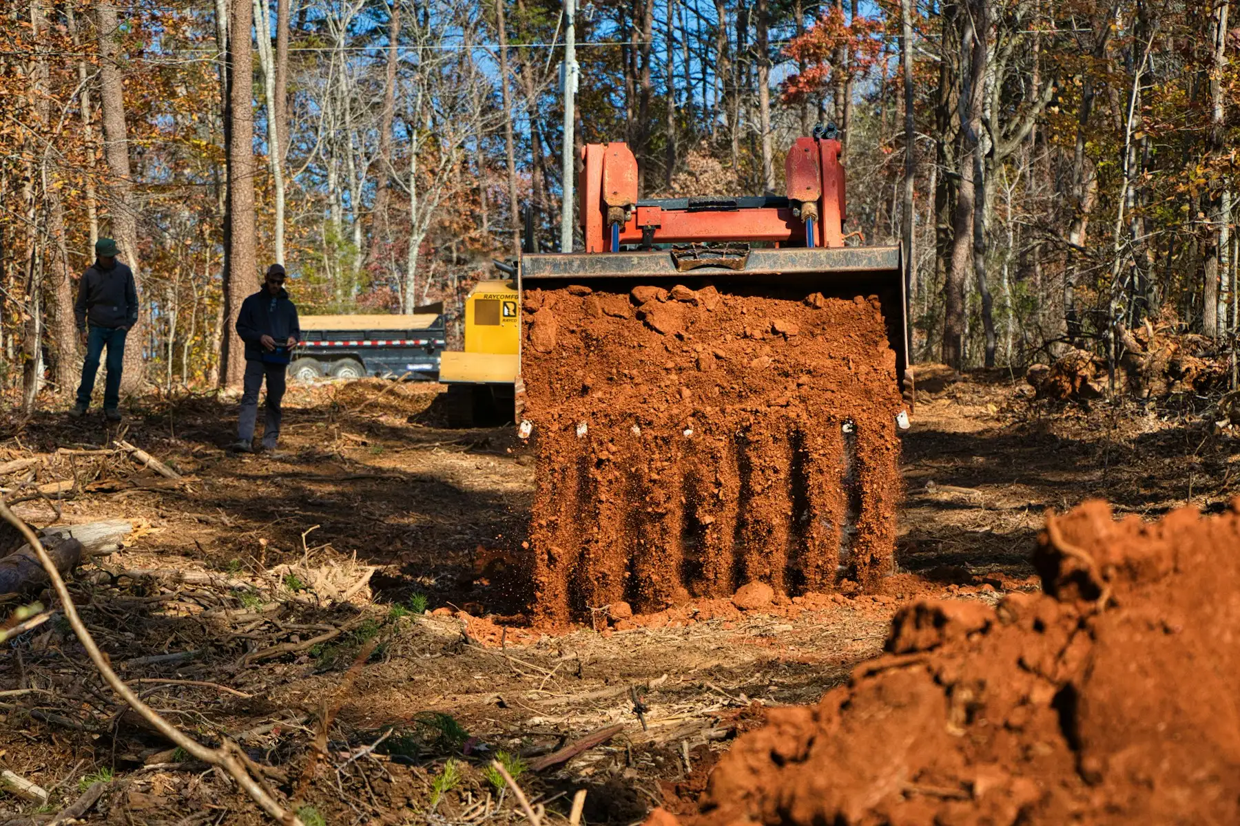 Excavator moving red clay on a wooded lot being cleared for building
