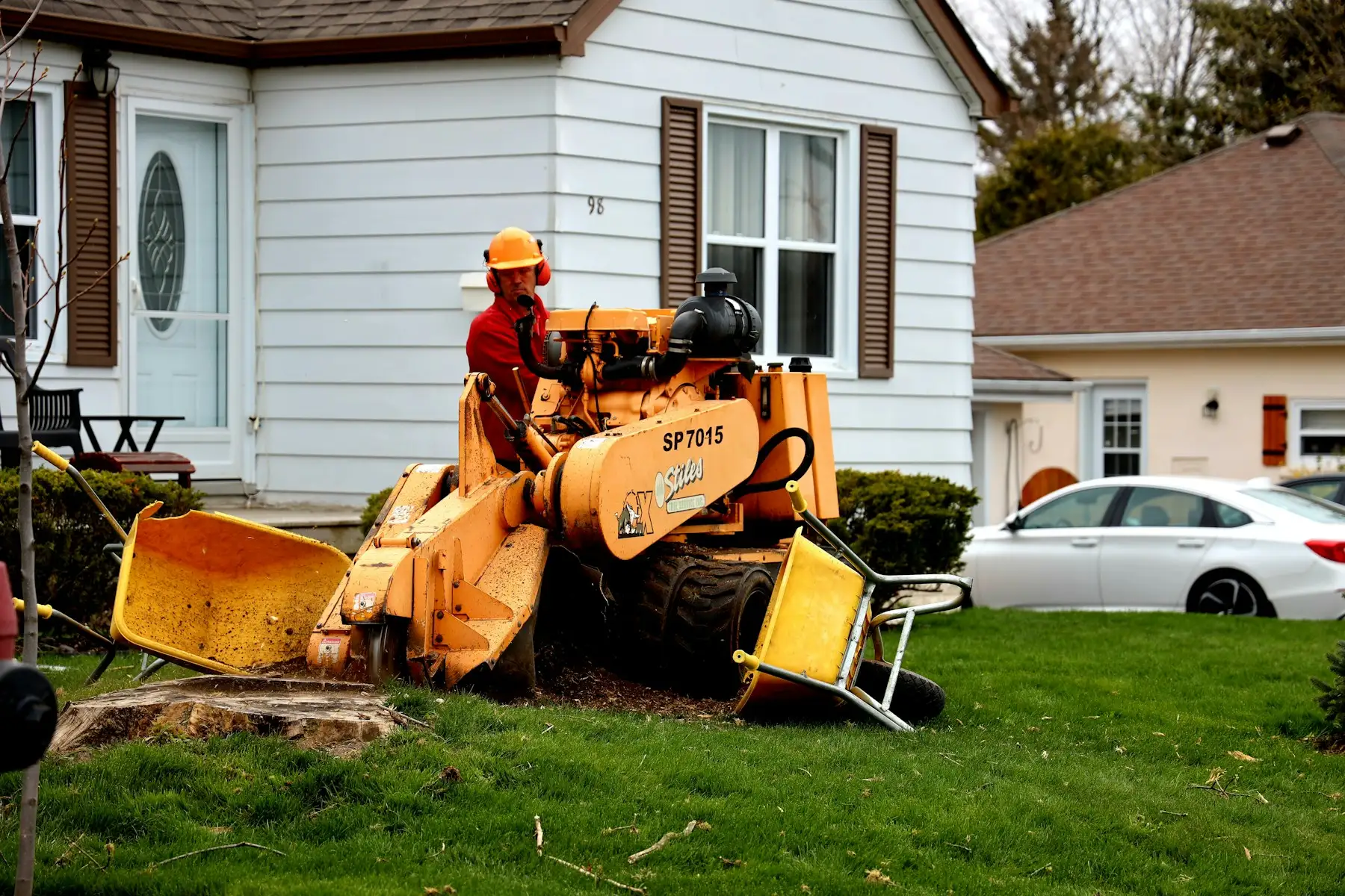 Operator running a stump grinder on a tree stump in a residential front yard